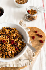 Bowl of homemade granola with nuts and fruits on white linen background. Side view