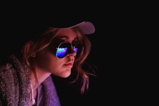 Hacker girl in a cap and sunglasses in front of a computer in neon light