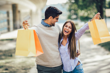 Portrait of happy couple with shopping bags after shopping in city smiling and holding credit card