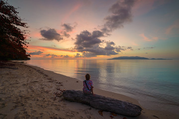 Fototapeta premium Woman relaxing on sand beach romantic sky at sunset, rear view, golden cloudscape, real people. Indonesia, Kei islands, Moluccas Maluku