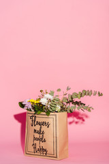 bouquet of flowers and eucalyptus leaves in paper bag with flowers make people happy lettering on...