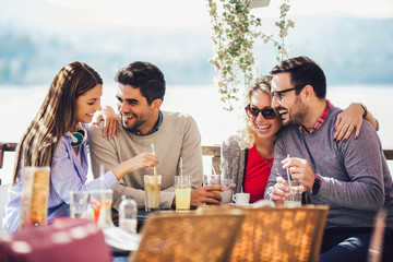 Group of four friends having fun a coffee together. Two women and two men at cafe talking laughing and enjoying their time