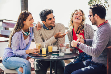 Group of four friends having fun a coffee together. Two women and two men at cafe talking laughing and enjoying their time