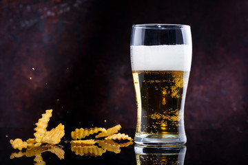 glass of beer with foam and chips on a dark background