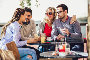Group of four friends having fun a coffee together. Two women and two men at cafe talking laughing and enjoying their time