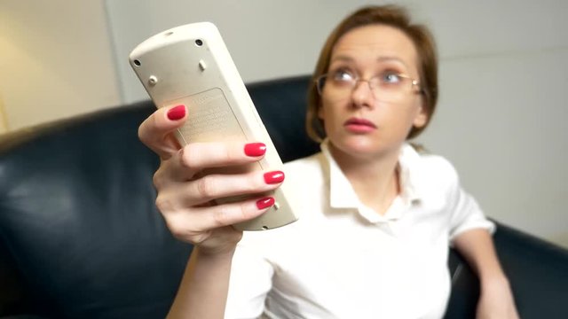 A business woman in a white blouse and red manicure unbuttons her shirt, and turns on the air conditioner with a remote control. close-up