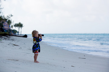 Mom, holding little toddler boy with binoculars, observing dolphins