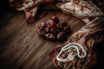 Dried apricots and dates fruit with wooden rosary on white wooden table. Top view.