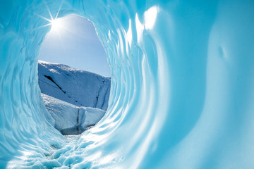 Sun shining into the entrance of a large round ice cave in the Matanuska Glacier in Alaska. - obrazy, fototapety, plakaty