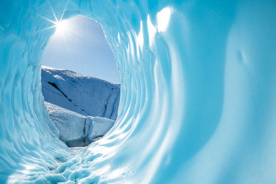 Sun shining into the entrance of a large round ice cave in the Matanuska Glacier in Alaska.