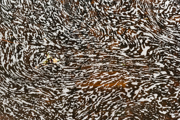 White foam on the water of a river moving through small waves making shapes of spirals and amorphous textures