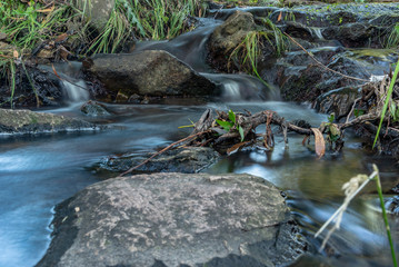 Small waterfall or cascade captured near the water surface full of rocks and plants with long exposure