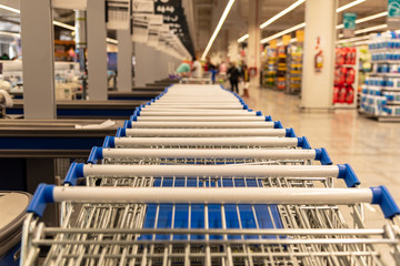 A lot of supermarket carts handles with shallow depth of field with a part of the market view blurred