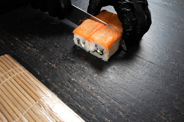Chef in black gloves prepare rolls on the black table in the kitchen