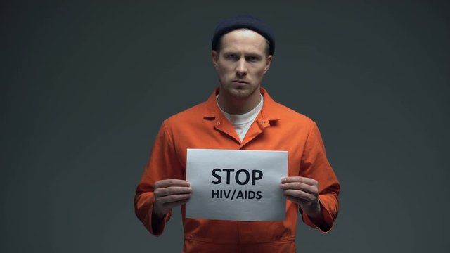 Imprisoned man holding Stop HIV AIDS sign in cell, sexually transmitted disease