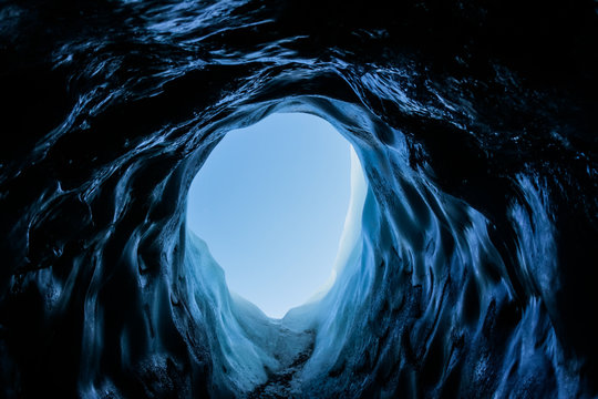 Small dark ice cave tunnel on the Matanuska Glacier in Alaska. The cave is dark but light shines on the clear ice inside.