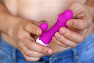 Dildo in male hands, sex toy. Man in jeans with naked torso holding purple silicone vibrator, concept of adult games, masturbation, stimulation