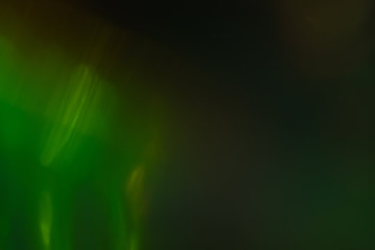 Blurred green abstract lens flare on dark background. Defocused glow effect.