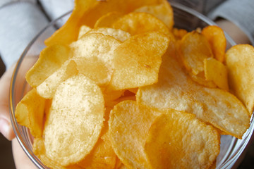 Chips close-up, in a glass container. A child holds a bunch of yellow chips.