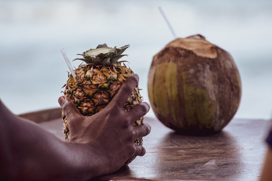 Dominican Man's Hand Holding A Pina Colada Cocktail Served In The Pineapple, In A Tropical Beach In The Dominican Republic. Vacation Concept.