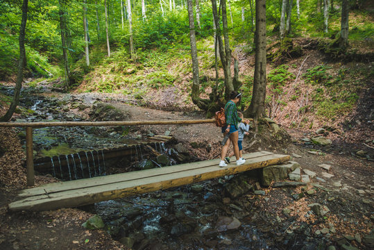 Mother With Kid Crossing River Via Bridge In Forest