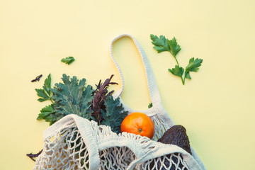 white eco-friendly textile string bag with fresh fruits, herbs and vegetables isolated on yellow...