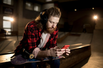 Portrait of bearded man using smartphone while sitting on ramp in extreme park, shot with flash