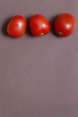 Three red fresh tomatoes lie on a brown background