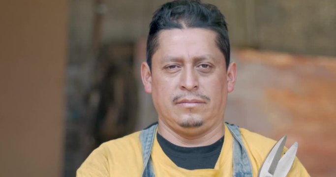 Hispanic male employee looking at the camera holding metal cutting sheers