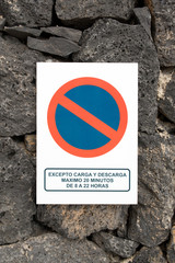 No parking sign mounted on stone wall with Spanish language that says ´except loading and...