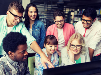 people, education, technology and school concept - group of happy smiling international students with computers at library in university