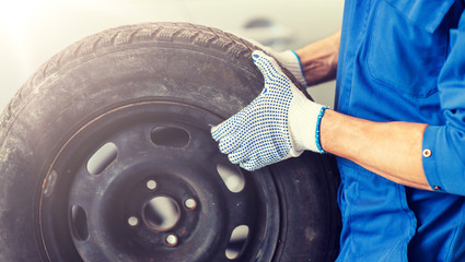 car service, repair, maintenance and people concept - auto mechanic man with wheel tire at workshop