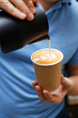Barista holding cardboard cup with cappuccino and pouring milk