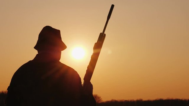 A hunter with a gun goes forward across the field towards the setting sun. Hobby for men
