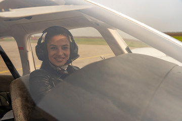 Smiling Young Woman Pilot With Headset Looking Through The Cockpit Window