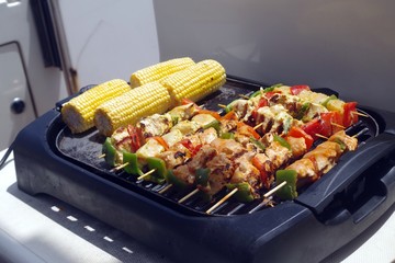 Picture of an electric barbecue topped with meat on skewers and vegetables that will be served as soon as cooked. Typical summer background.