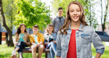 teen and people concept - smiling teenage girl with long hair in denim jacket over her friends on summer background