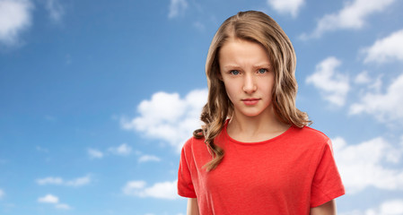 emotion, expression and people concept - sad or angry teenage girl in red t-shirt over blue sky and...