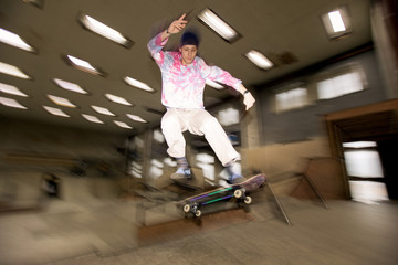 Action shot of young man doing skating stunt flying in air at skateboard park, shot with flash