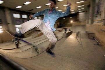 Action shot of contemporary young man doing skating stunt on ramp at skateboard park, shot with...