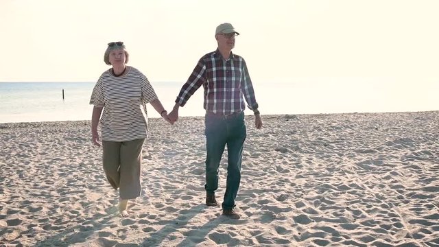 fr&ouml;hliches, gl&uuml;ckliches, verliebtes Rentner Ehepaar, Senioren gehen am Strand spazieren. Alte Frau, alter Mann