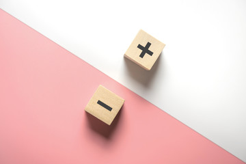 The concept of opposites, wood blog with plus and minus  on white and pink background, flat lay,...