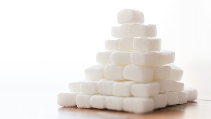 food, junk-food, cooking and unhealthy eating concept - close up of white lump sugar pyramid on wooden table