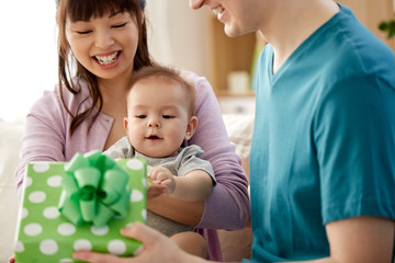 mixed-race family, parenthood and mothers day concept - happy mother, father and baby son with gift box at home