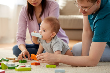 mixed-race family, parenthood and people concept - happy mother, father and baby boy playing toy blocks at home