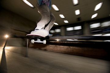 Action shot of unrecognizable young man doing skating stunt flying in air at skateboard park, shot with flash