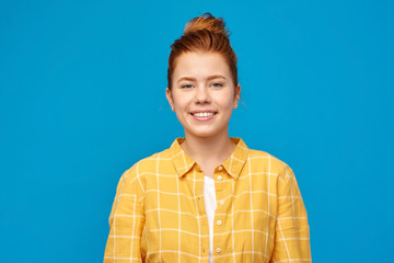 people concept - smiling red haired teenage girl in checkered shirt over bright blue background