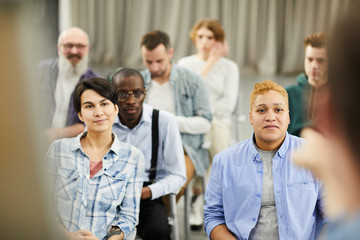 Group of content curious people in casual clothing sitting on chairs and listening to speaker...