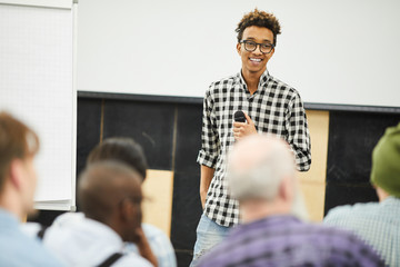 Positive successful young African-American entrepreneur in glasses standing in front of audience...