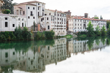 Fototapeta na wymiar white houses along river Brenta in Bassano del Grappa, Italy. With reflection in water